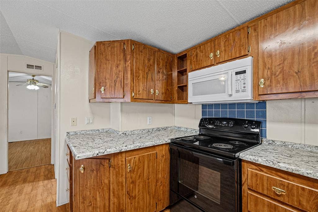 Kitchen featuring wood-finish cabinetry, stone-patterned countertops, a blue tile backsplash, and a black electric range with a mounted microwave