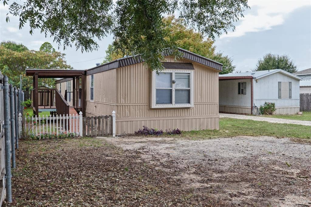 Exterior features include a metal-sided facade, a covered porch, a white picket fence, and a gravel driveway