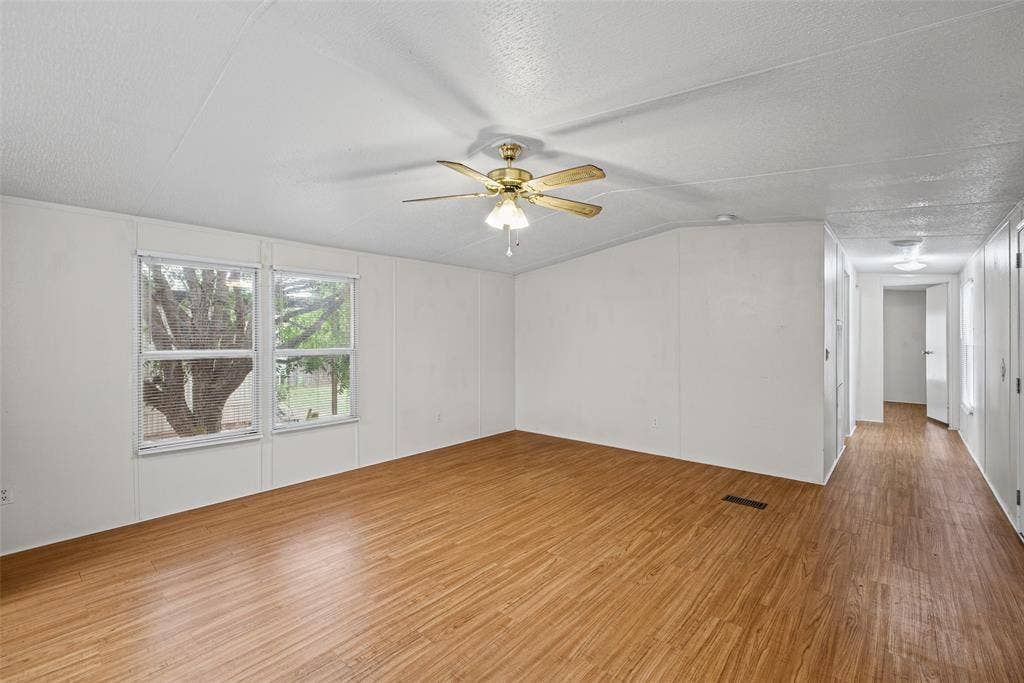 Spacious room featuring wood-finish flooring, dual windows, a ceiling fan with light fixture, and textured ceilings