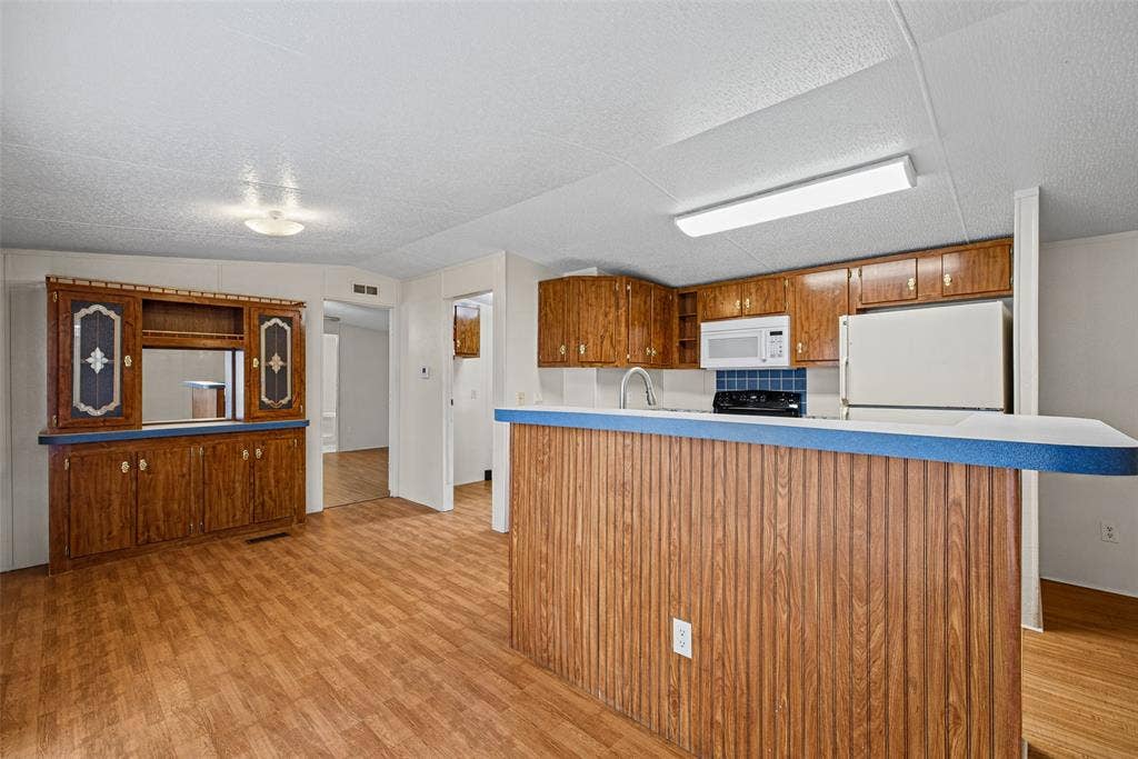Kitchen featuring wood cabinetry, a peninsula with a laminate countertop, wood-finish flooring, built-in microwave, and decorative glass-front display hutch