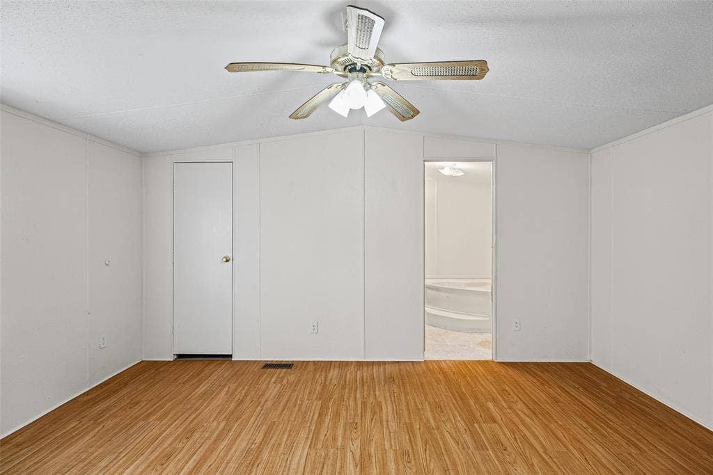 Wood-finish flooring, central ceiling fan with multi-light fixture, and neutral wall paneling