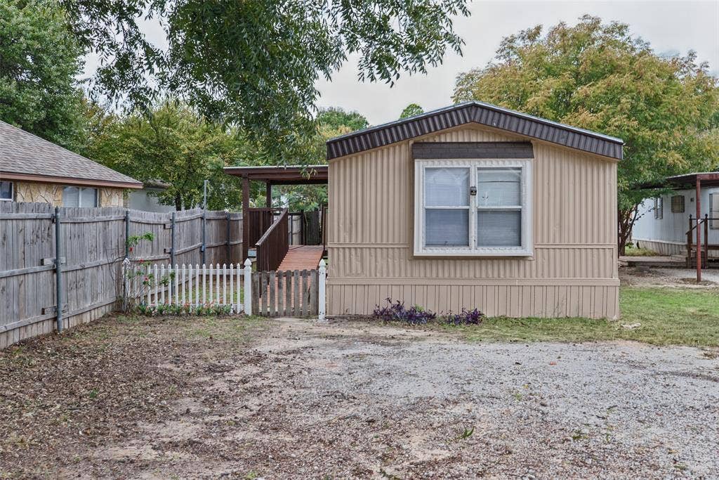 Exterior featuring metal siding, a covered entry ramp, and a white picket fence enclosing a portion of the yard
