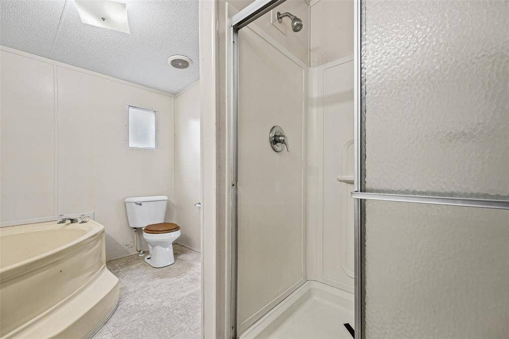Bathroom featuring a corner soaking tub, a separate shower stall with a framed sliding glass door, a toilet, and neutral-toned flooring