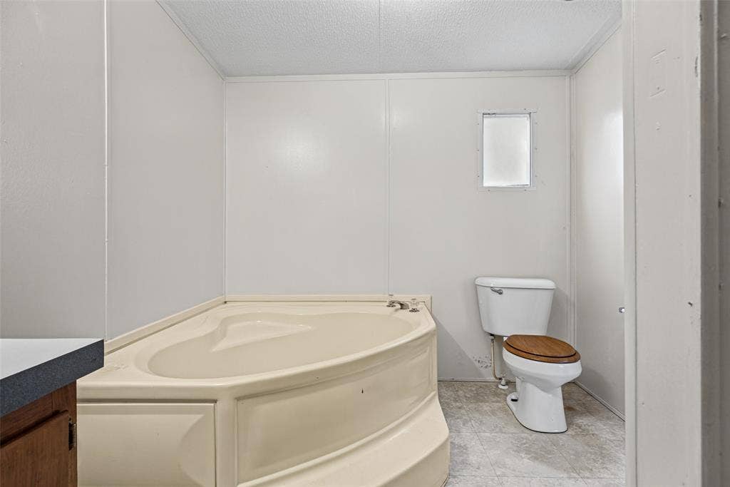 Corner soaking tub with integrated stairs, white porcelain toilet, and neutral-tone flooring