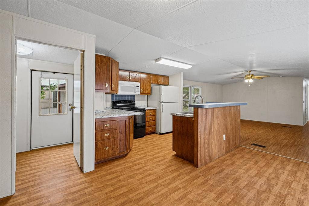 Kitchen featuring wood cabinetry, stone-finish countertops, a central peninsula with a breakfast bar, wood-finish flooring, and a ceiling fan