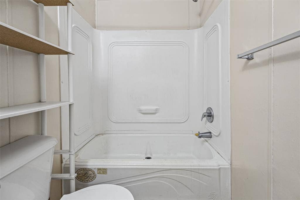 White acrylic tub-and-shower surround with integrated molded shelving, chrome-finish single-handle faucet, and attached metal towel bar