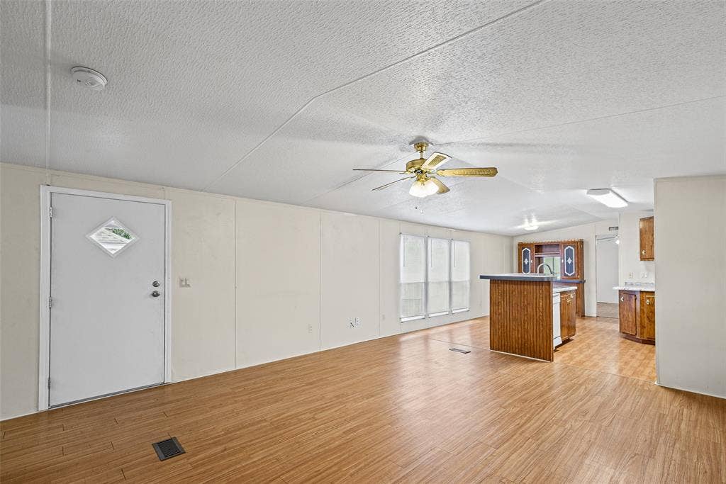 Open-concept interior featuring wood-finish flooring, a kitchen island with built-in cabinetry, ceiling-mounted lighting, and a multi-paneled entry door with a diamond-shaped window