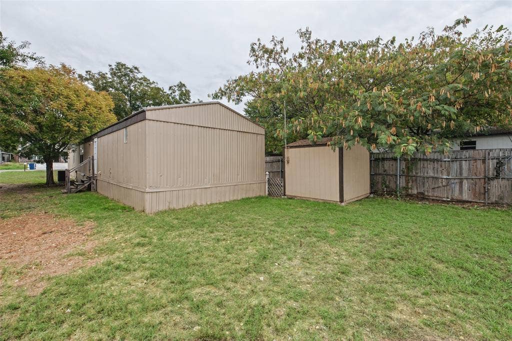 Exterior lot featuring metal siding, a detached storage structure, wooden perimeter fencing, and mature trees