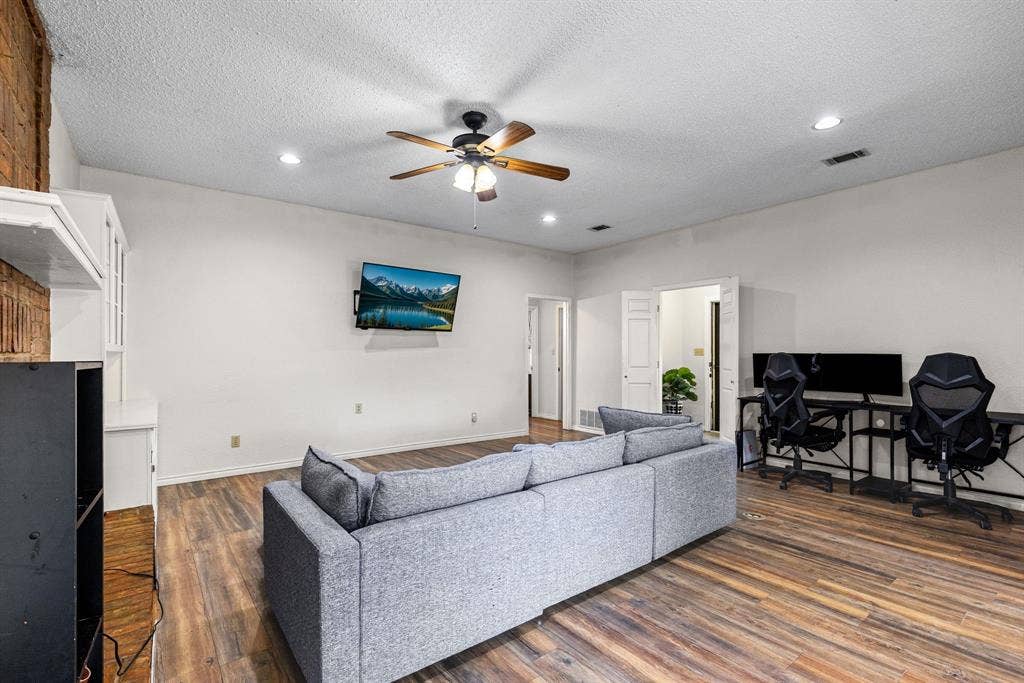 1307 Edna Street, Commerce, TX 75428 Living area featuring wood-finish flooring, a textured ceiling with a central fan, recessed lighting, and a brick-accented wall with built-in cabinetry