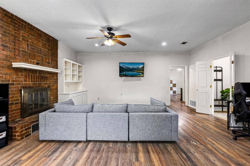 1307 Edna Street, Commerce, TX 75428 Full-height brick fireplace with a mantle and built-in shelving, wood-finish flooring, and a ceiling fan with integrated lighting