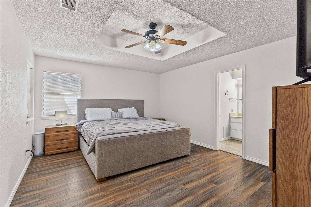 1307 Edna Street, Commerce, TX 75428 Bedroom featuring a tray ceiling with a central multi-blade ceiling fan and wood-finish flooring
