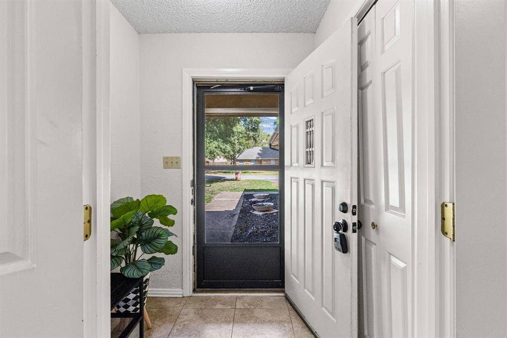 1307 Edna Street, Commerce, TX 75428 Entryway featuring a white paneled door with a decorative inset window, a glass-panel storm door, and neutral tile flooring