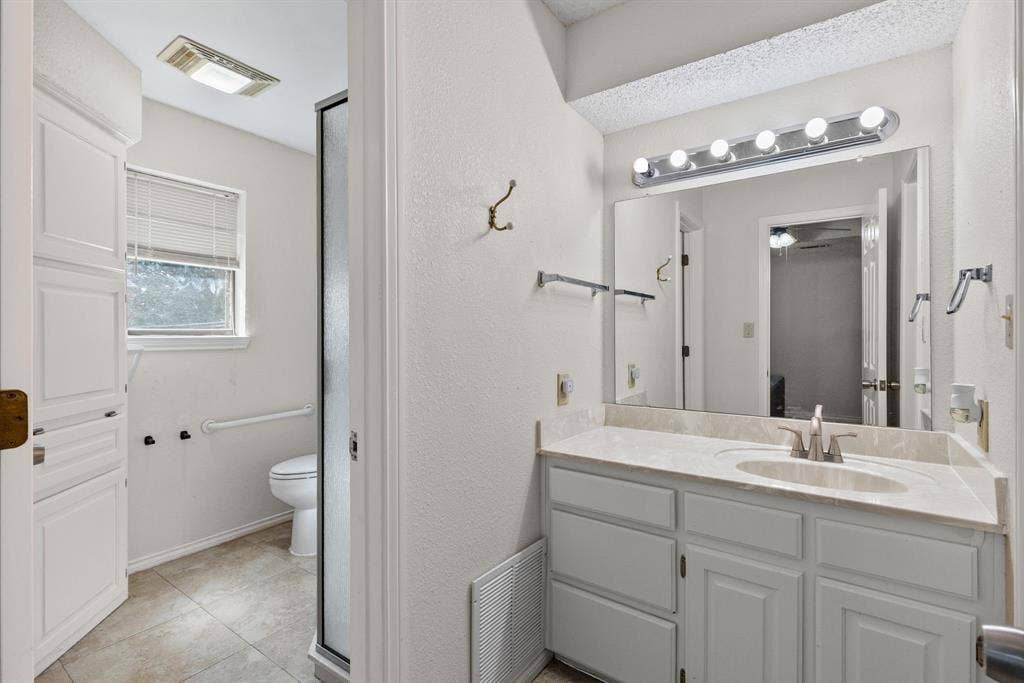 1307 Edna Street, Commerce, TX 75428 Bathroom featuring a vanity with white cabinetry, a single-basin sink, a multi-bulb vanity light, and large-format tile flooring