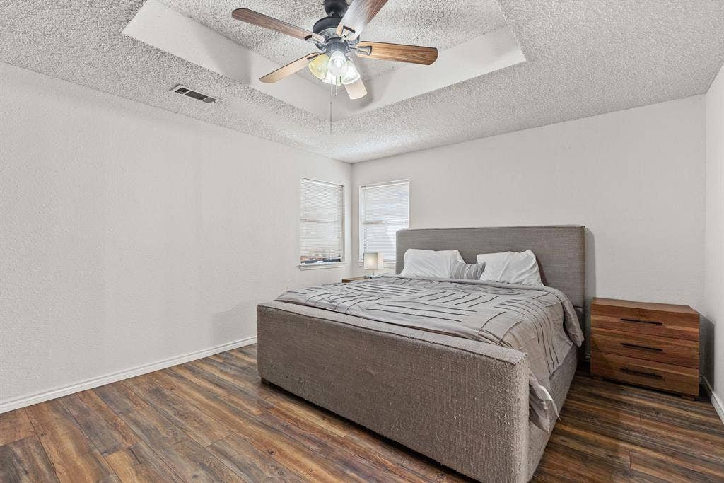 1307 Edna Street, Commerce, TX 75428 Room featuring wood-finish flooring, a tray ceiling with a center-mounted ceiling fan, and dual windows