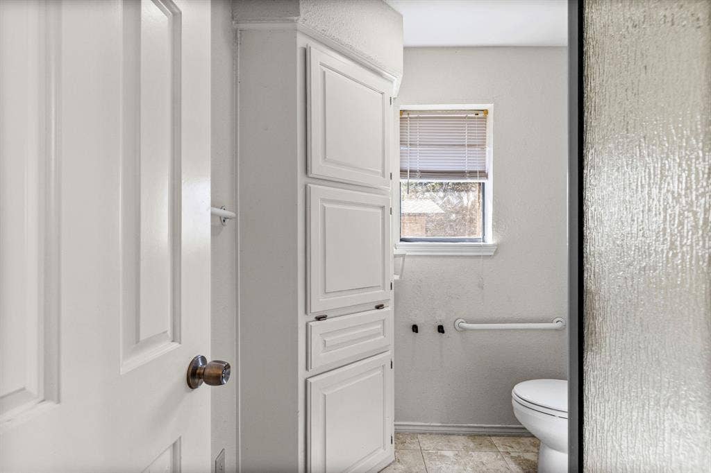 1307 Edna Street, Commerce, TX 75428 Built-in floor-to-ceiling cabinetry, neutral tile flooring, and wall-mounted grab bar
