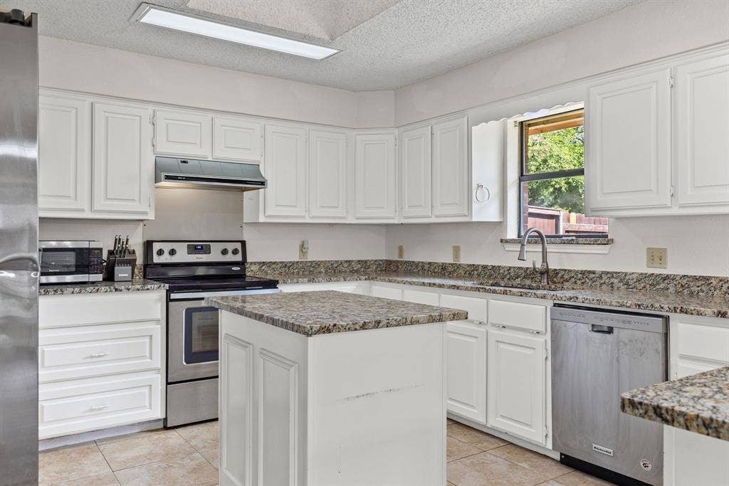 1307 Edna Street, Commerce, TX 75428 Kitchen featuring white shaker-style cabinetry, stone-finish countertops, central island, stainless steel appliances, and tile flooring