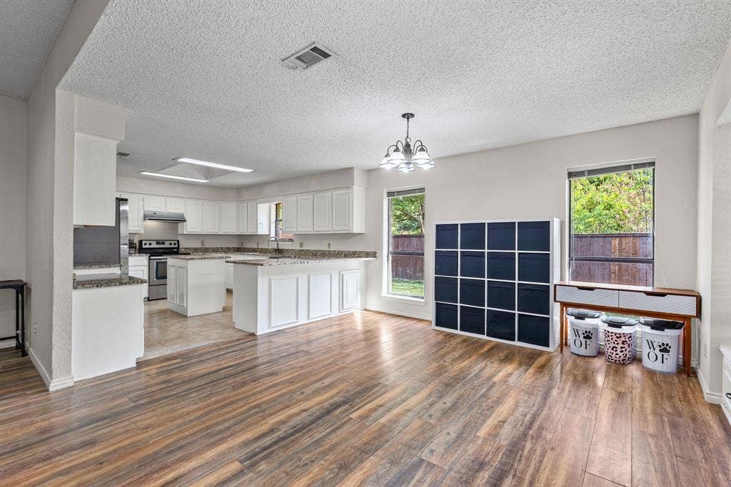 1307 Edna Street, Commerce, TX 75428 Open-concept kitchen and living area featuring wood-finish flooring, white cabinetry, stone-surface countertops, and multi-pane windows