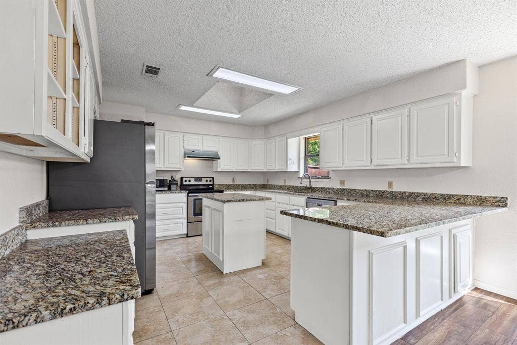 1307 Edna Street, Commerce, TX 75428 Kitchen featuring white shaker-style cabinetry, stone-finish countertops, a center island, recessed lighting, and tile flooring