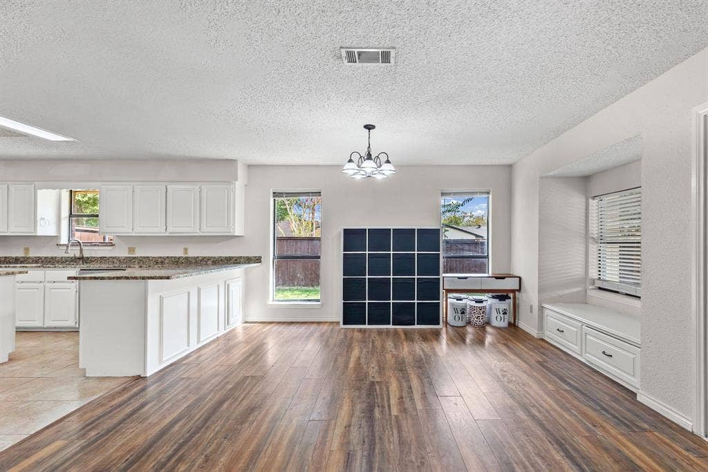 1307 Edna Street, Commerce, TX 75428 Kitchen area featuring white cabinetry, stone-surface countertops, wood-finish flooring, a multi-arm chandelier, and a built-in window seat with storage drawers