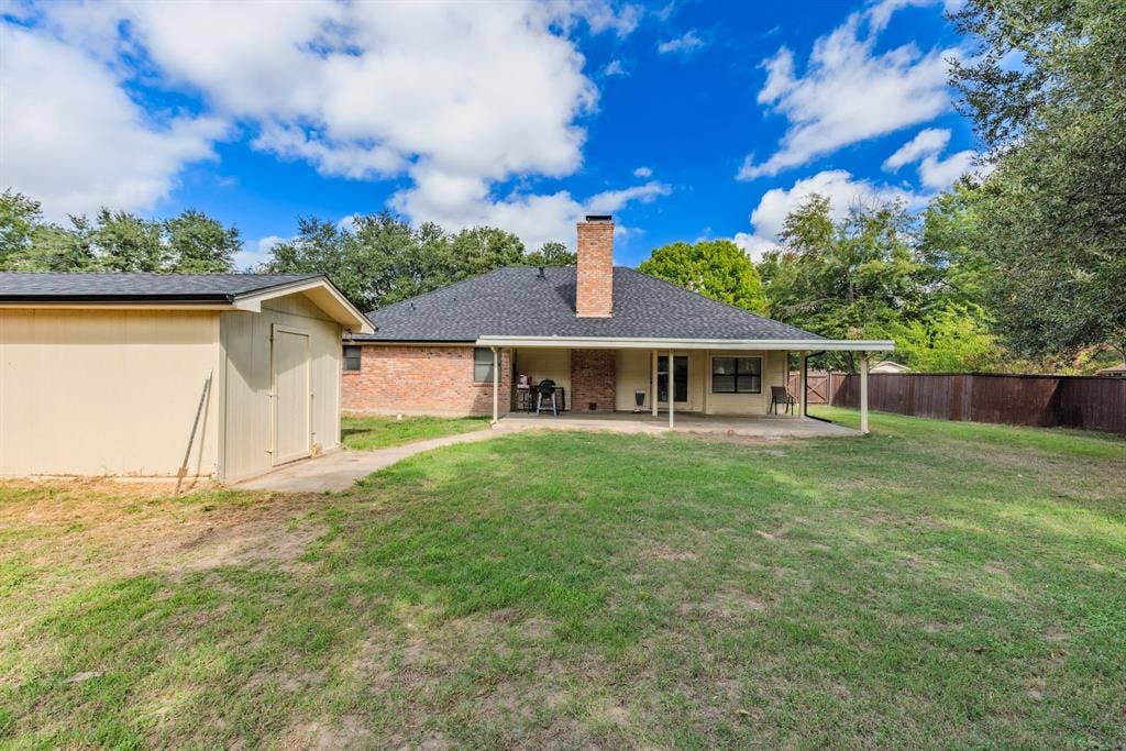 1307 Edna Street, Commerce, TX 75428 Expansive backyard featuring a covered patio, brick exterior chimney, detached storage building, and perimeter wood fencing