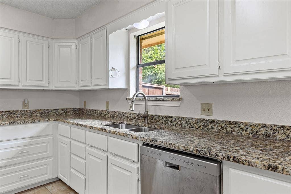 1307 Edna Street, Commerce, TX 75428 Kitchen featuring white cabinetry, stone-finish countertops, stainless steel dual-basin sink with pull-down faucet, and integrated dishwasher