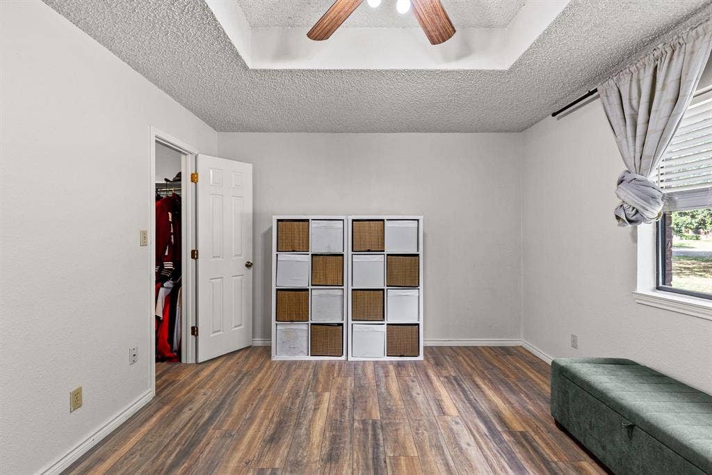 1307 Edna Street, Commerce, TX 75428 Interior space featuring wood-finish flooring, tray ceiling, and a ceiling fan