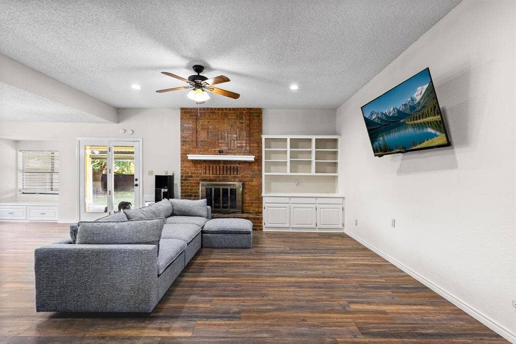 1307 Edna Street, Commerce, TX 75428 Living area featuring wood-finish flooring, floor-to-ceiling brick fireplace with wood mantel, built-in white shelving, recessed lighting, and sliding glass doors