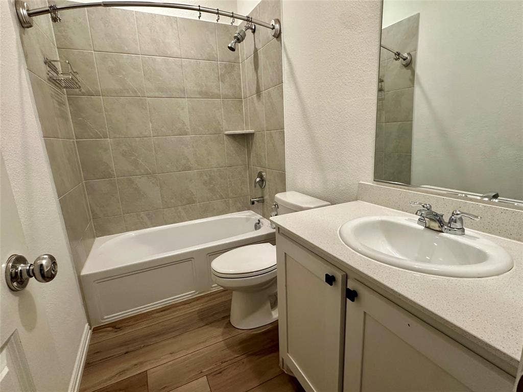 Bathroom featuring wood-finish flooring, vanity with light-toned solid surface countertop, inset sink, and tub-shower combination with full-height tile surround