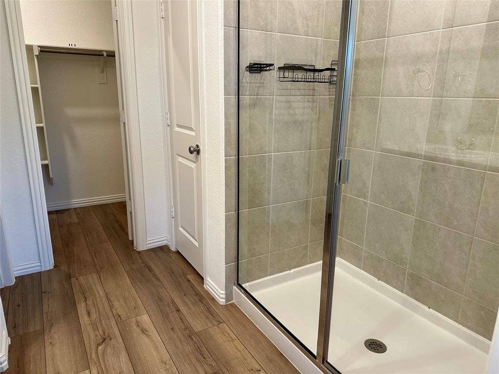 Shower stall with a glass enclosure, tile surround, and built-in shelving, complemented by wood-finish flooring and an integrated closet featuring built-in storage shelving