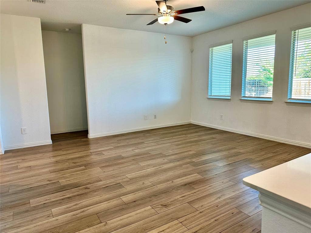 Interior space featuring wood-finish flooring, three windows with horizontal blinds, and a ceiling fan with integrated lighting