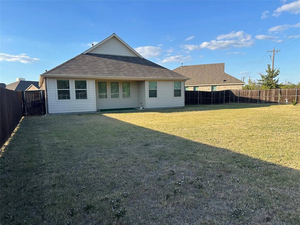 Expansive backyard featuring a leveled lawn, tall wood-panel privacy fencing, and exterior siding with a gabled roofline