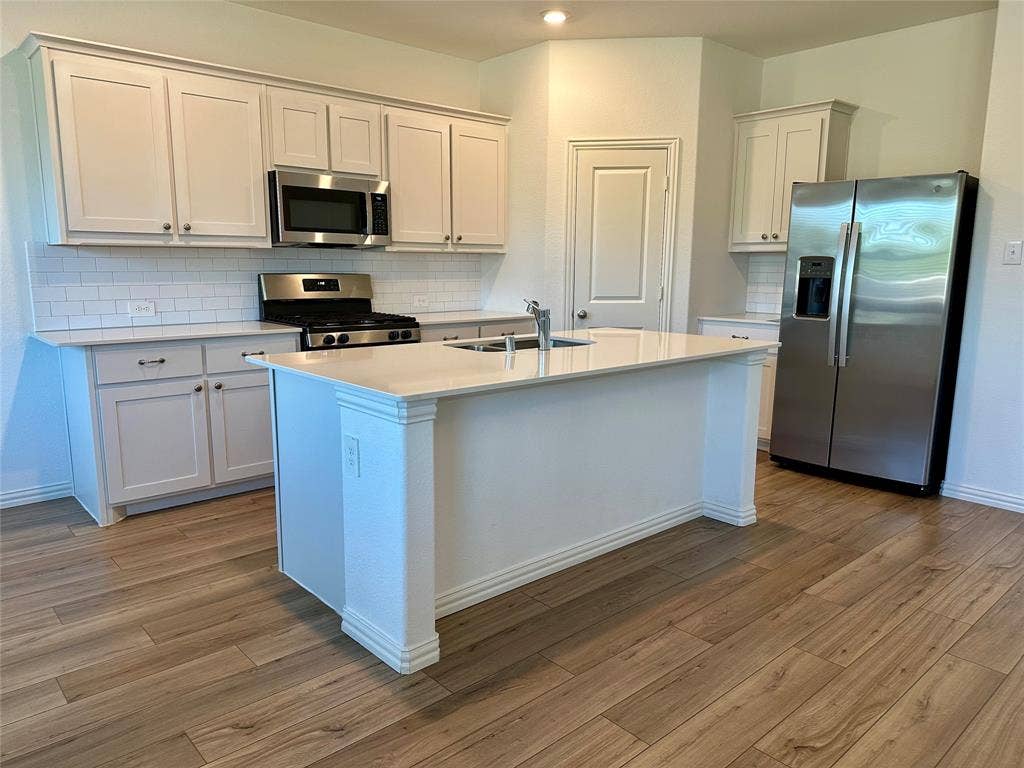 Kitchen featuring white shaker-style cabinetry, a central island with a solid-surface countertop, white subway tile backsplash, stainless steel appliances, and wood-finish flooring