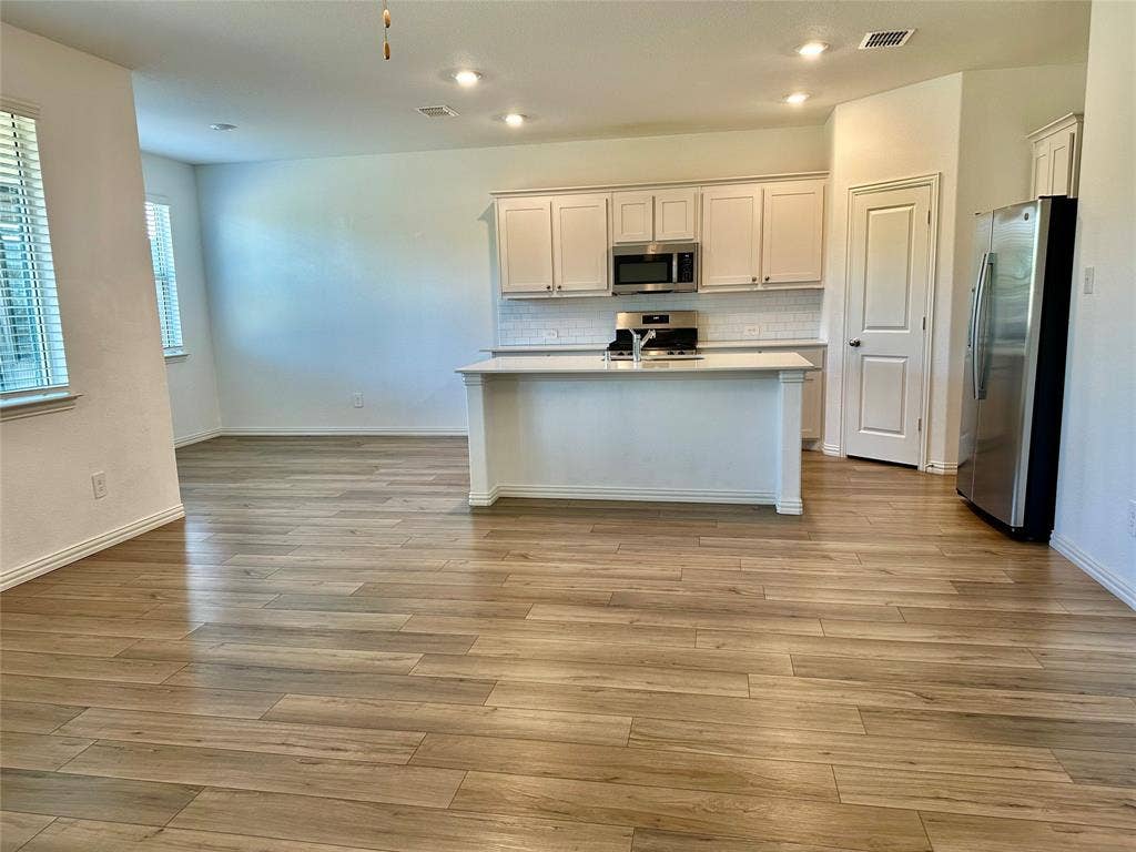 Kitchen featuring white cabinetry, quartz-topped center island, wood-finish flooring, stainless steel appliances, and subway tile backsplash