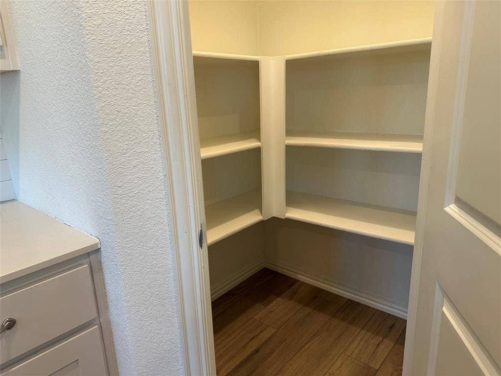Walk-in storage space featuring wood-finish flooring and multiple tiers of built-in shelving