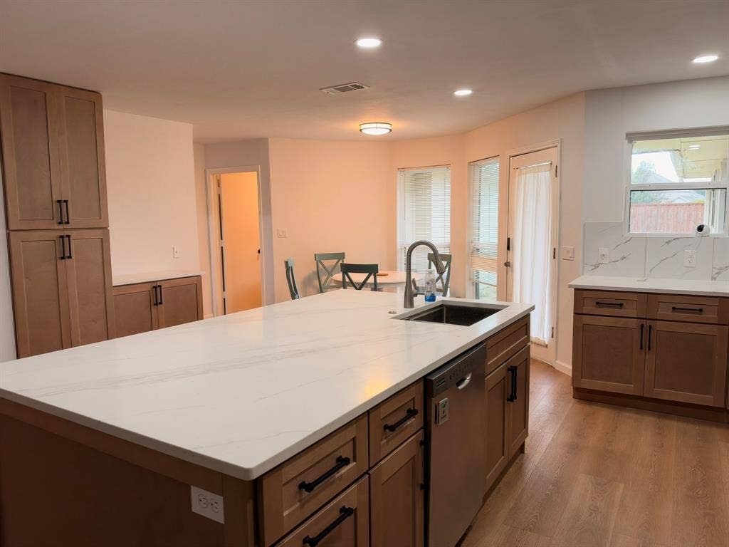 Kitchen featuring a central island with a solid-surface countertop, wood-finish cabinetry, recessed lighting, wood-finish flooring, and a stone-look tile backsplash