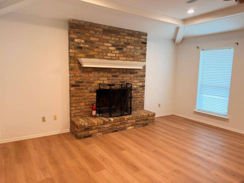 Floor-to-ceiling brick fireplace with an elevated hearth and white mantle, featuring wood-finish flooring and a tray ceiling