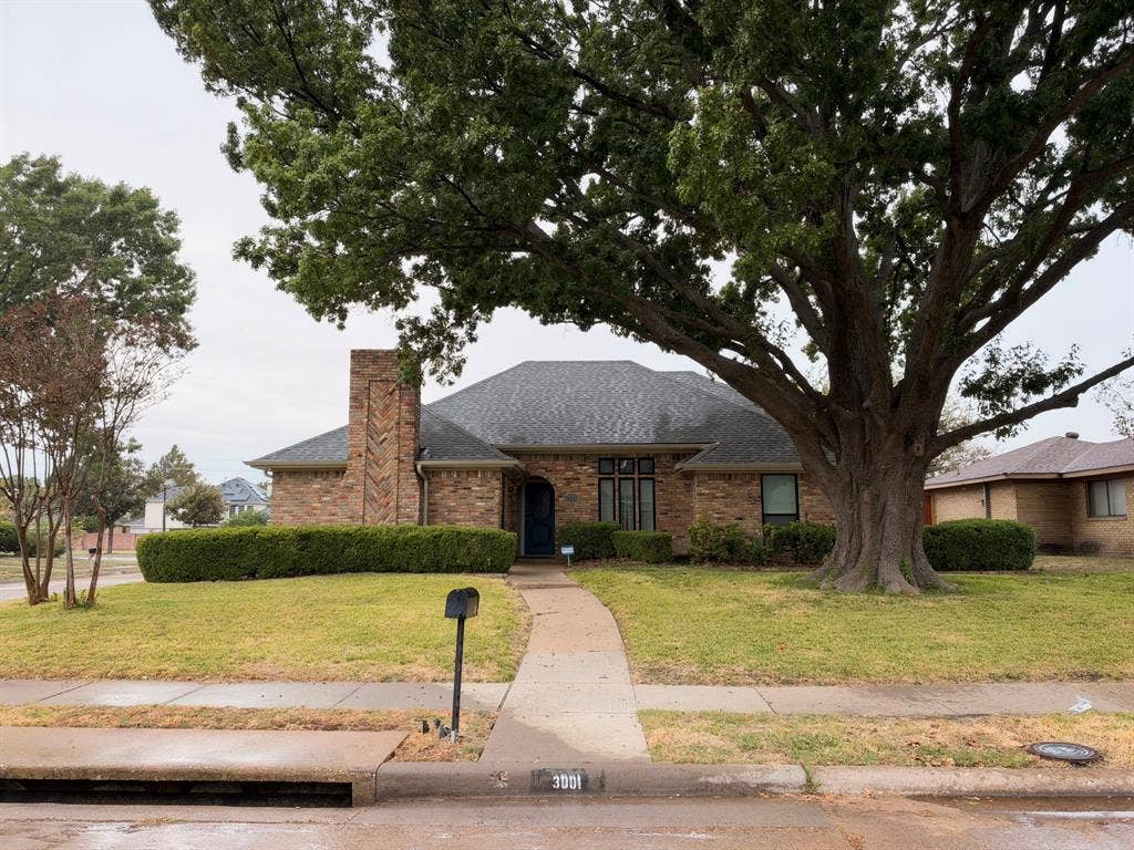 Single-story brick exterior featuring a prominent chimney with herringbone masonry detailing, hipped roofline, and mature landscaping