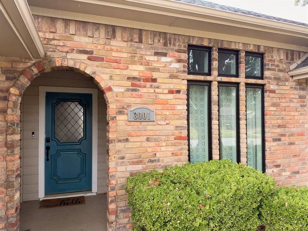 Exterior featuring a multi-tonal brick facade, arched entryway, solid door with leaded-glass inset, and a triple-pane window arrangement with black framing