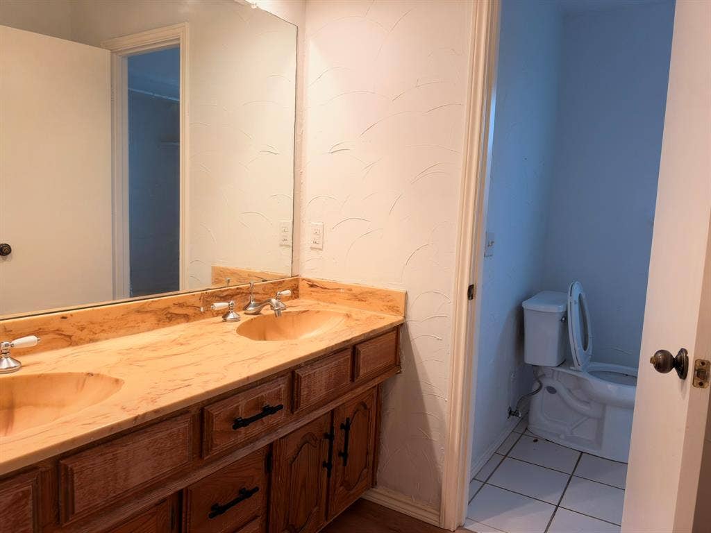 Double vanity featuring wood cabinetry, integrated dual sinks, a full-width mirror, and tile flooring