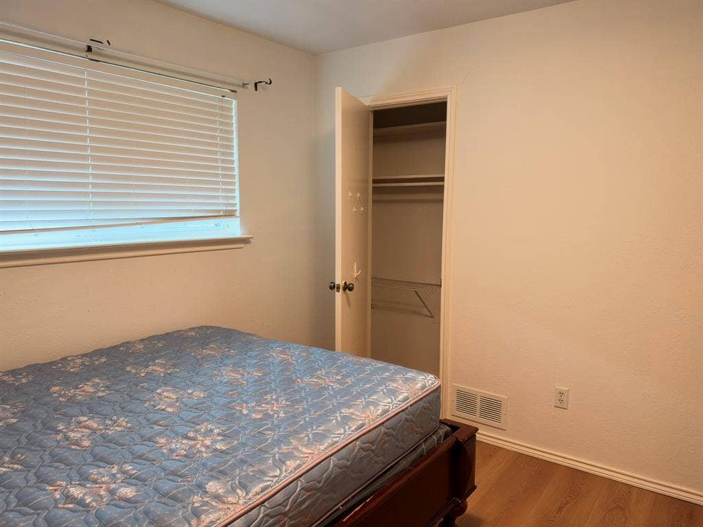 Room featuring wood-finish flooring, a neutral color palette, a window with horizontal blinds, and a reach-in closet with built-in shelving