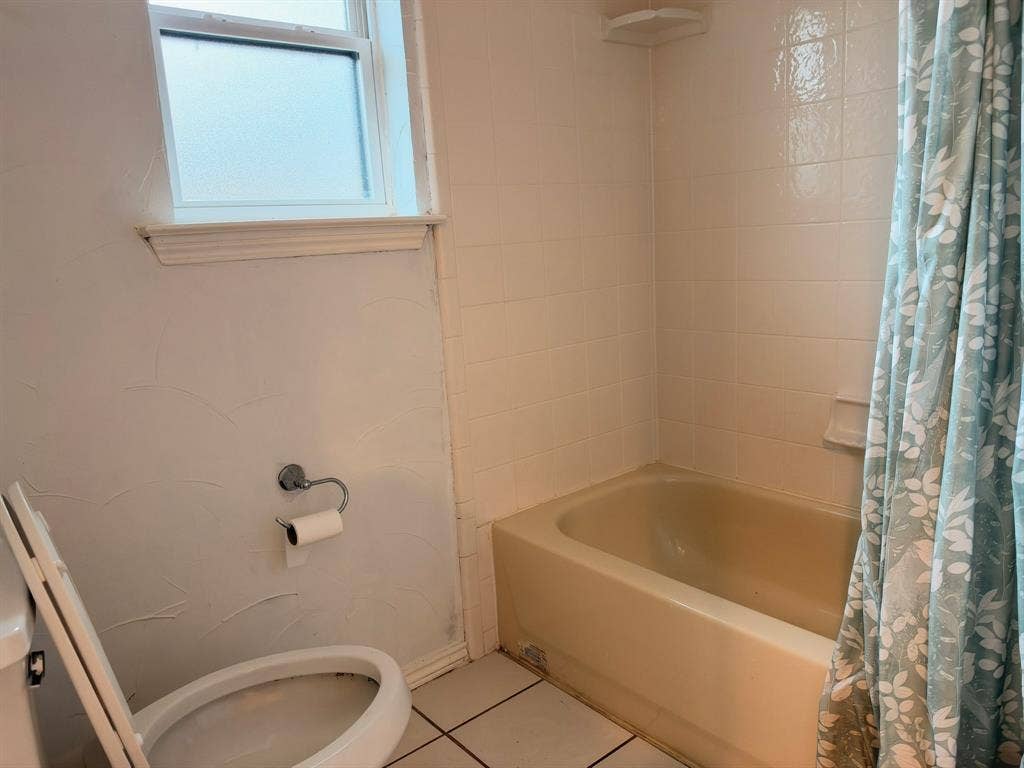 Bathroom featuring a porcelain bathtub, square-tile wall surround, frosted glass window, and ceramic floor tiling