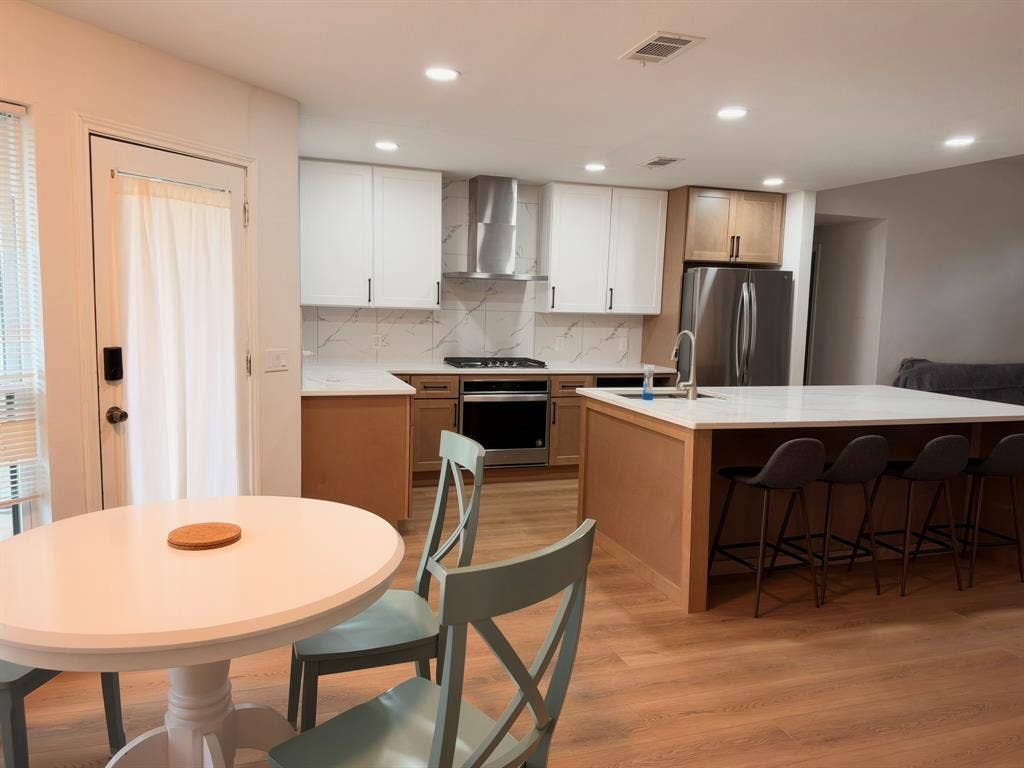 Kitchen featuring two-tone cabinetry, stainless steel appliances, quartz countertops, a matching backsplash, and a central island with integrated sink