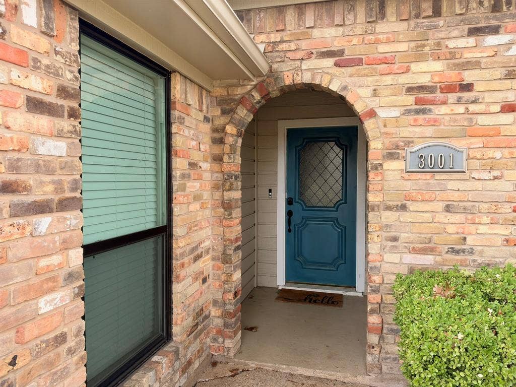 Multi-colored brick exterior featuring an arched entryway, recessed porch, decorative paneled front door with diamond-patterned glass, and custom house number plaque