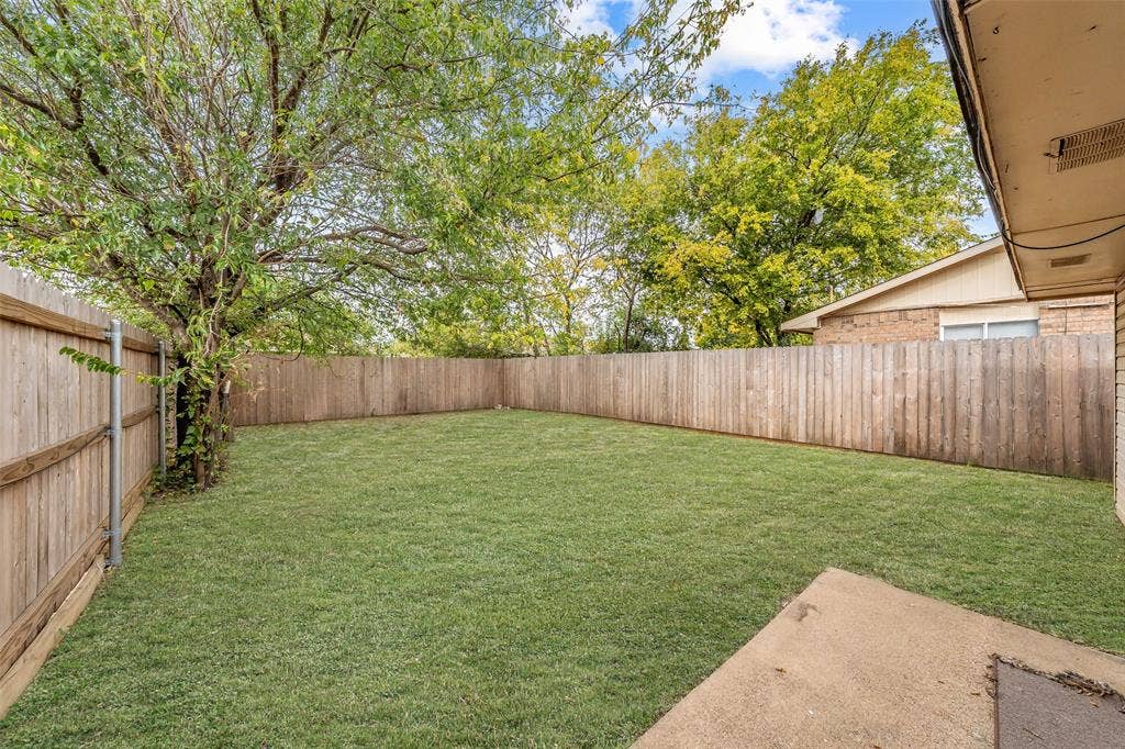 1128 Backyard featuring a grass lawn, wood perimeter fencing, concrete patio, and mature trees