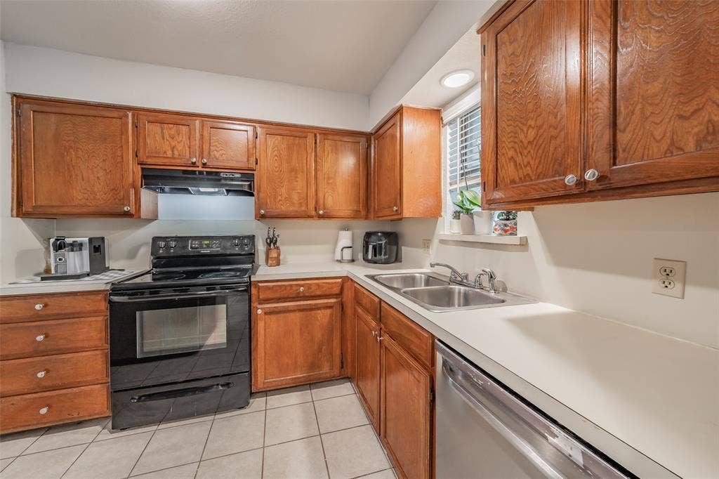 1128 Kitchen featuring stained wood cabinetry, solid surface countertops, ceramic tile flooring, a dual-basin stainless steel sink, and integrated black appliances