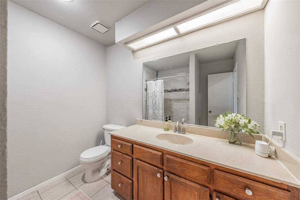 1128 Full-width vanity with natural-finish wood cabinetry, integrated stone-composite countertop, oval basin, large wall-mounted mirror, and tile flooring
