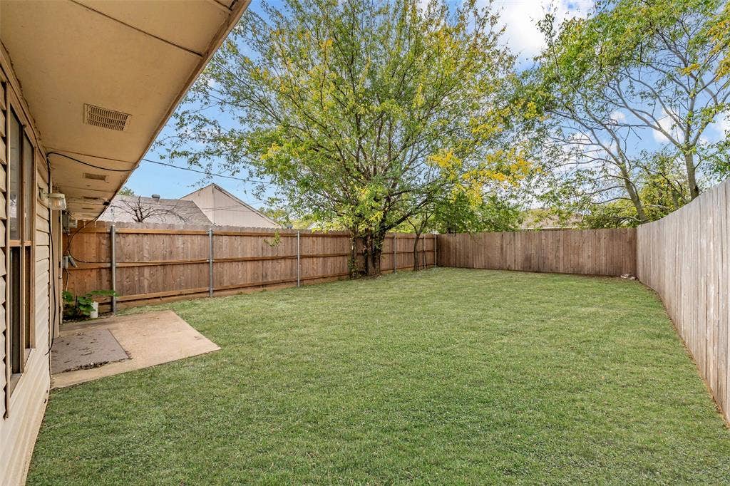 1128 Backyard featuring a grass lawn, concrete patio, wood privacy fencing, and mature trees