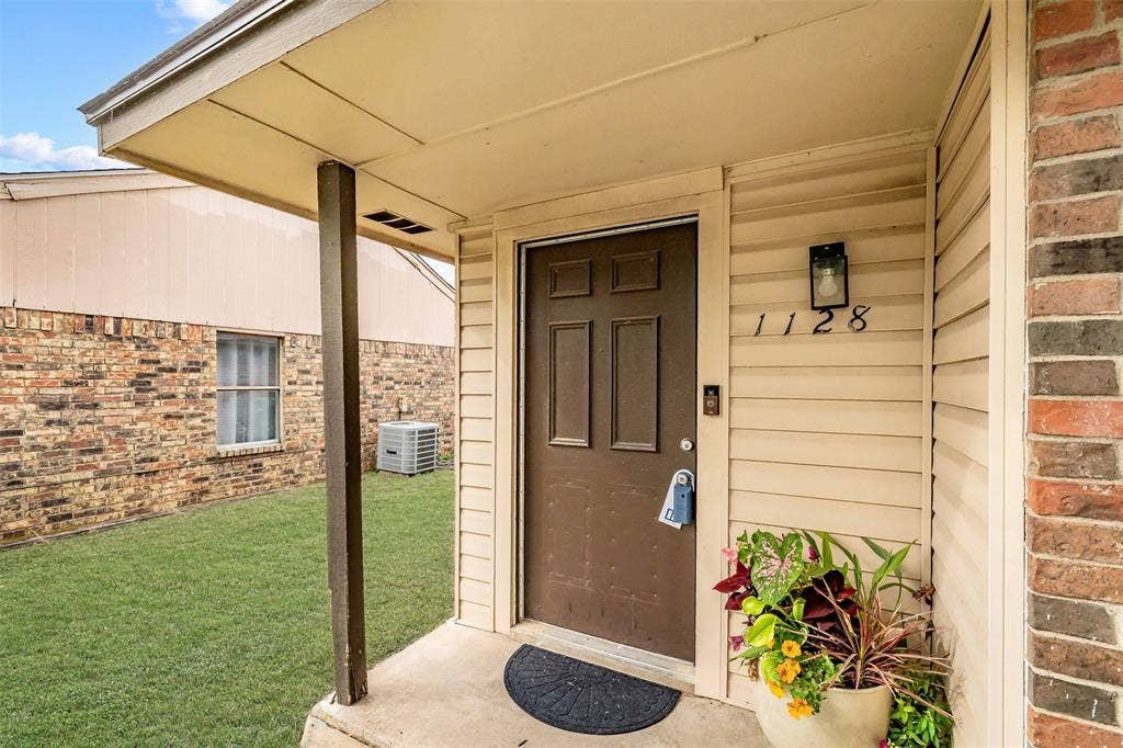 1128 Covered entryway featuring a six-panel door, horizontal siding, brick exterior accents, and an attached exterior light fixture