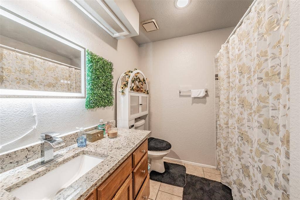 1126 Bathroom featuring a stone-pattern vanity countertop, an undermount sink with a chrome single-handle faucet, a large rectangular backlit vanity mirror, and recessed ceiling lighting