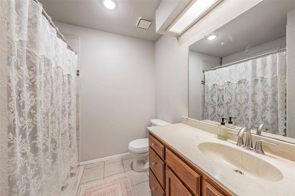 1128 Bathroom featuring a wood-finish vanity with a stone-composite countertop, integrated oval basin, recessed lighting, and a large-format mirror
